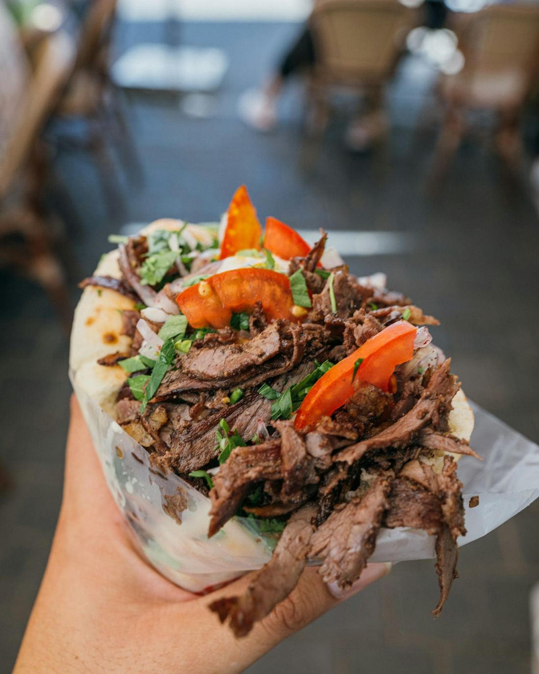 A shawarma wrap loaded with carved meat, salad and sauce, held in one hand