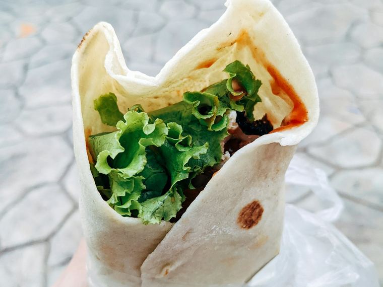 An open wrap filled with chicken and fresh greens